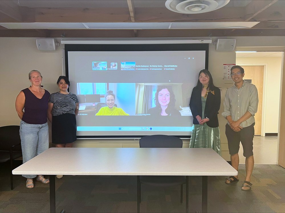 Group photo taken after the defense, with committee members in the room and two more joining on the screen behind